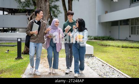 Eine Gruppe fröhlicher, vielfältiger asiatischer Universitätsstudenten unterhalten sich gern, während sie gemeinsam den Fußweg im Campus-Park entlang laufen. Universität li Stockfoto