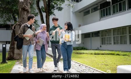 Eine Gruppe fröhlicher, vielfältiger asiatischer Universitätsstudenten unterhalten sich gern, während sie gemeinsam den Fußweg im Campus-Park entlang laufen. Universität li Stockfoto