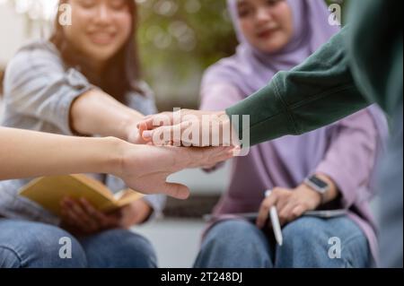 Das Bild einer Gruppe fröhlicher, vielfältiger asiatischer Universitätsstudenten legt die Hände zusammen, ermutigt und unterstützt sich gegenseitig A Stockfoto