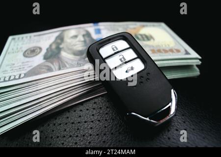 Autoschlüssel oder schlüssellose Fernbedienung und usd-Dollar-Banknoten auf einem schwarzen Ledersitz im Auto. Kauf- und Autokredit-Konzept Stockfoto