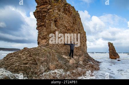 Ein Mann steht an großen Felsen am Cullen-Strand, wenn die Flut hereinkommt Stockfoto