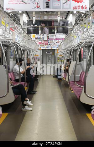 Eine U-Bahn-Fahrt in Tokio mit dem Zug der Odeo-Linie. Alle Passagiere schauen auf ihre Telefone. Stockfoto