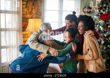 Aufgeregte multiethnische Familie begrüßt Großeltern am ersten Weihnachtsfeiertag. Eine glückliche Familie für mehrere Generationen Stockfoto