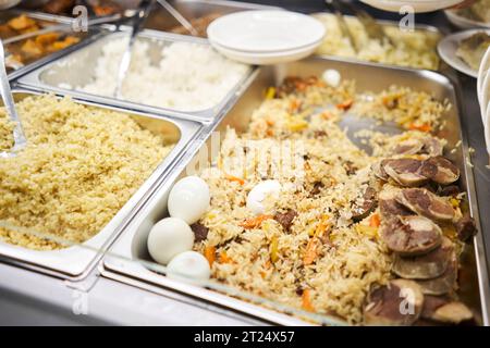 Ein traditionelles usbekisches Gericht namens Pilaf. Reis mit Fleisch, Karotten, Zwiebeln, Wachteleiern und Kazy. Glasvorführung in einem Buffet oder Selbstbedienungsrestaurant. Stockfoto
