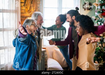 Aufgeregte multiethnische Familie begrüßt Großeltern am ersten Weihnachtsfeiertag. Eine glückliche Familie für mehrere Generationen Stockfoto