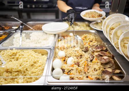 Ein traditionelles usbekisches Gericht namens Pilaf. Reis mit Fleisch, Karotten, Zwiebeln, Wachteleiern und Kazy. Glasvorführung in einem Buffet oder Selbstbedienungsrestaurant. Stockfoto