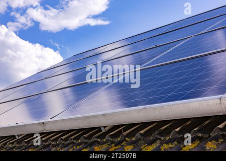Solarpaneele einer Photovoltaikanlage auf einem Privatwohnheim mit verunreinigten Dachziegeln auf dem Dach des Hauses gegen Wolken Stockfoto