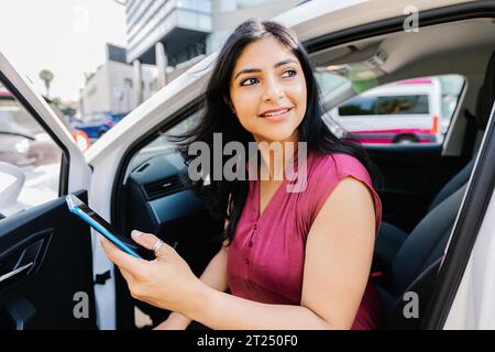 Eine junge indianerin, die ein Handy hält und auf dem Auto sitzt Stockfoto