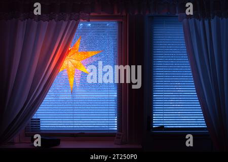 Ein Adventsstern, Weihnachtslichter im Fenster. Verschneite Fenster, Vorhänge und ein Radio. Wald im Freien. Stockfoto