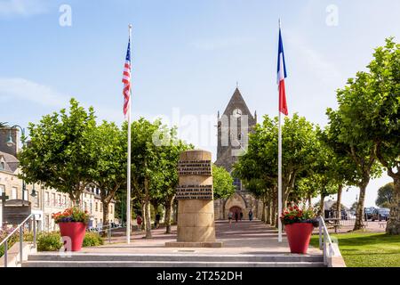 Befreiungsdenkmal mit der Kirche Sainte-Mere-Eglise in der Ferne, zum Gedenken an die Befreiung des Dorfes durch amerikanische Fallschirmjäger am D Day. Stockfoto