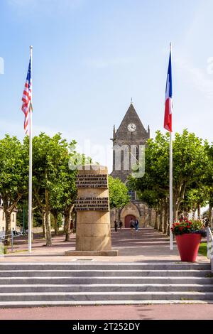 Befreiungsdenkmal mit der Kirche Sainte-Mere-Eglise in der Ferne, zum Gedenken an die Befreiung des Dorfes durch amerikanische Fallschirmjäger am D Day. Stockfoto