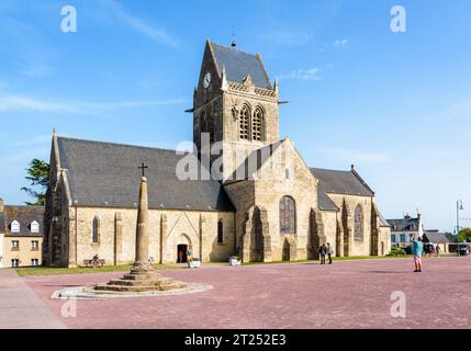 Allgemeine Ansicht der Kirche von Sainte-Mere-Eglise mit einer Fallschirmspringerpuppe, die am Turm hing, als Hommage an das, was der Privatmann John Steele am D Day durchmachte Stockfoto