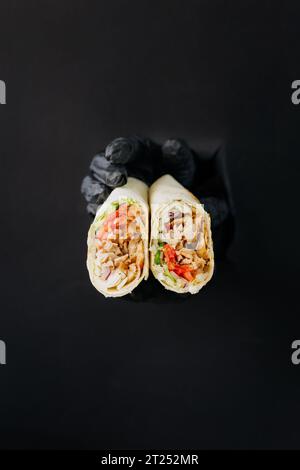 Hände, die Döner oder Shawarma durch gerissene Löcher auf schwarzem Papierhintergrund halten. Street-Food-Konzept Stockfoto