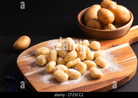 Food Concept Spot Focus hausgemachte Gnocchi auf Holzbrett auf schwarzem Hintergrund mit Kopierraum Stockfoto