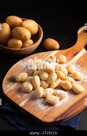 Food Concept Spot Focus hausgemachte Gnocchi auf Holzbrett auf schwarzem Hintergrund mit Kopierraum Stockfoto