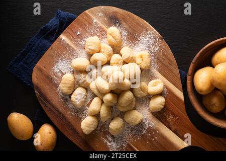 Food Concept Spot Focus hausgemachte Gnocchi auf Holzbrett auf schwarzem Hintergrund mit Kopierraum Stockfoto