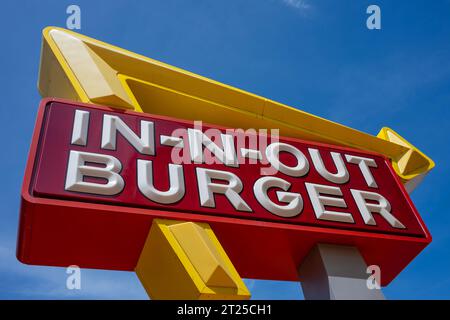 SAN FRANCISCO, USA - 21. April 2023: Niedriger Winkel des roten Schilds mit den Buchstaben IN-N-OUT BURGER und dem gelben Pfeil, der die Richtung gegen wolkenlos zeigt Stockfoto