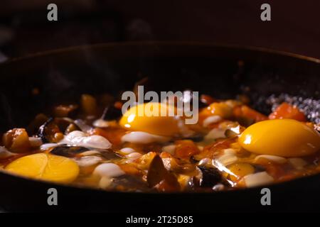 Nahaufnahme von Hühnereiern, Tomaten und Auberginen in einer Pfanne gebraten. Kochprozess, selektiver Fokus. Hausgemachte Speisen zum Frühstück Stockfoto