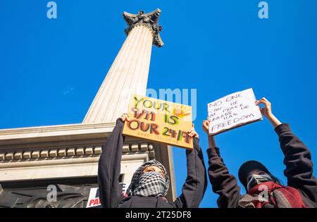 London, Großbritannien. 14. Oktober 2023: Zwei maskierte pro-palästinensische Demonstrantinnen halten Plakate auf dem Trafalgar Square, London, bei einer Demonstration gegen Israel Stockfoto