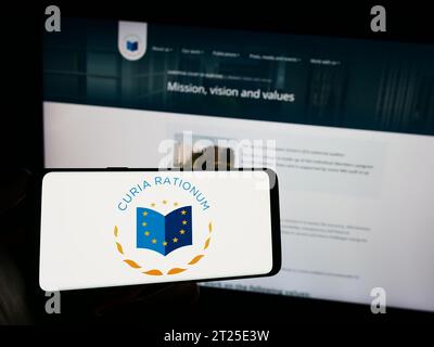 Person mit Mobiltelefon mit Logo des EU-Organs Europäischer Rechnungshof (EuRH) vor der Webseite. Schwerpunkt auf dem Display des Telefons. Stockfoto