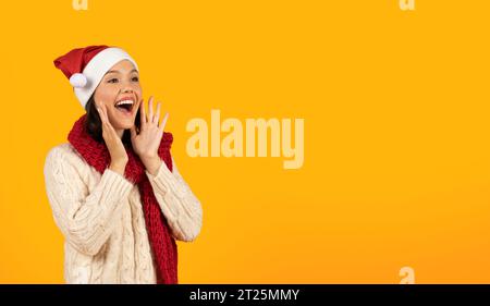 Aufgeregte Junge Frau Mit Weihnachtsmütze, Die Beiseite Schaut, Gelber Hintergrund Stockfoto