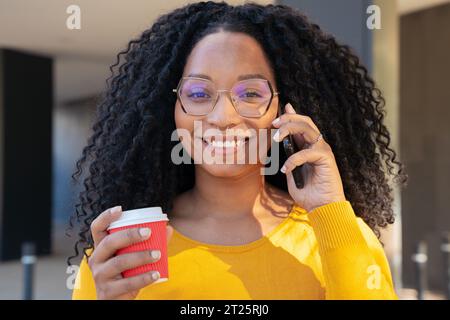 Porträt Junge lächelnde schwarze Frau am Handy beim Kaffeetrinken. Stockfoto