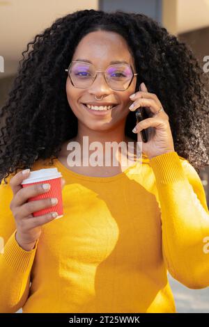 Nahaufnahme Porträt lächelnde schwarze Frau am Handy, während sie Kaffee trank. Stockfoto
