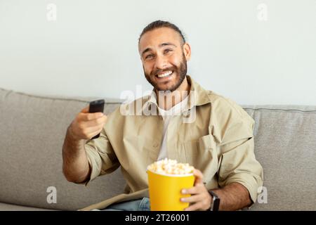 Entspannter Millennial-Mann, der zu Hause Freizeit verbringt und fernsieht Stockfoto