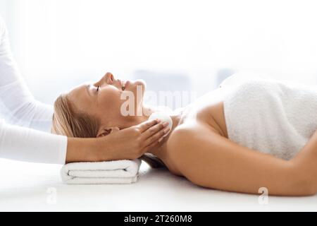 Heitere Frau mittleren Alters, die eine hautreinigende Behandlung durch professionelle Kosmetikerin erlebt Stockfoto