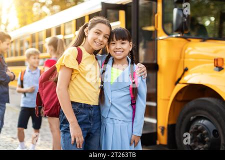 Glückliche Kinder posieren in der Nähe des Schulbusses, bereit nach dem Unterricht nach Hause zu gehen Stockfoto