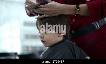 Little Boy wird vom professionellen Friseur im Friseursalon geschnitten und gekämmt, Person mit Haartrockner Stockfoto