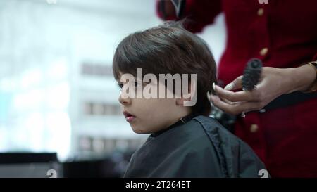 Little Boy wird vom professionellen Friseur im Friseursalon geschnitten und gekämmt, Person mit Haartrockner Stockfoto