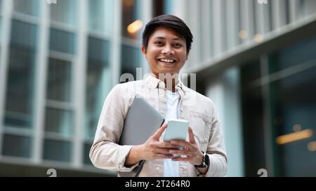 Glücklicher asiatischer Manager, der ins Büro geht, telefonisch Stockfoto