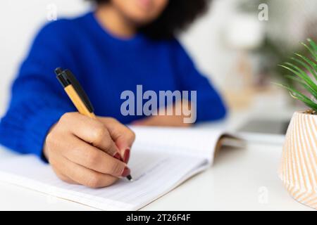 Nahaufnahme einer jungen Frau, die Notizen in einem Notebook macht, während sie zu Hause mit dem Notebook arbeitet Stockfoto
