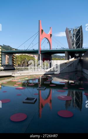 „L'Arc rouge“ (der rote Bogen) auf der La Salve-Brücke, die sich in einem Teich vor dem Guggenheim-Kunstmuseum in Bilbao, Spanien, spiegelt. Stockfoto