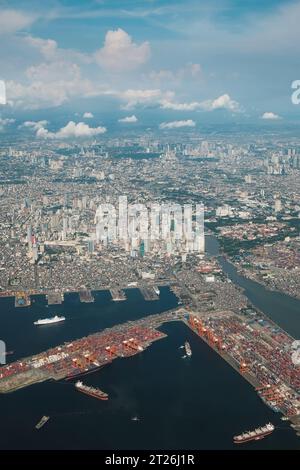 Luftaufnahme der Stadt Manila. Hauptstadt der Philippinen vom Flugzeug oben. Bucht von Manila, Schiffe, Hafen, Pasig River, Gebäude darunter, Wolken im blauen Himmel. Stockfoto