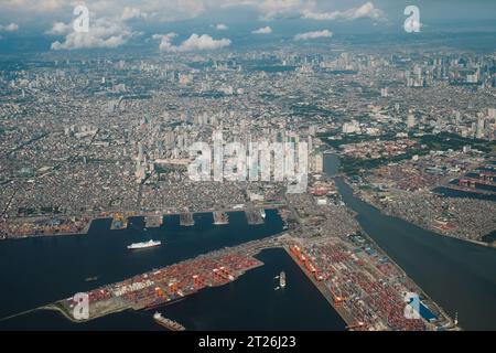 Luftaufnahme der Stadt Manila. Hauptstadt der Philippinen vom Flugzeug oben. Bucht von Manila, Schiffe, Hafen, Pasig River, Gebäude darunter, Wolken im blauen Himmel. Stockfoto