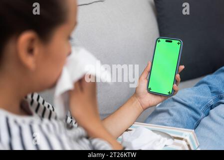 Kranke Frau mit laufender Nase kommuniziert mit dem Arzt über ein Mobiltelefon mit Chromakey-Bildschirm Stockfoto