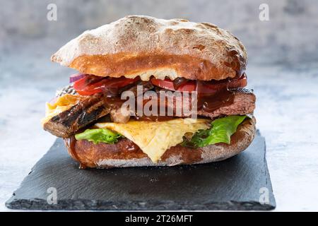 Brötchen mit Rinderrumpsteak, frischen Tomaten, Zwiebeln, grünem Salat, brauner Suppe und einigen Makrosprossen. Stockfoto