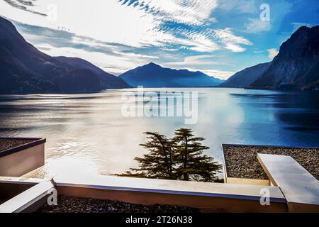 Fantastischer alter Park neben dem Wasser des Luganer Sees - Dach mit Kieselsteinen in der Ferne Brücke der Auto-Straße (oder Eisenbahn). Blick vom Olivenpfad (Lugano Vorort Stockfoto