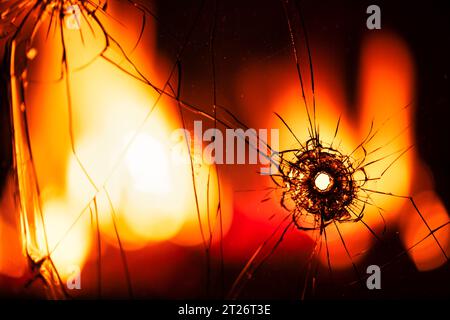 Eruption of Destruction: Ein Kugelloch, das zwischen Flammen durch Glas durchbricht Stockfoto