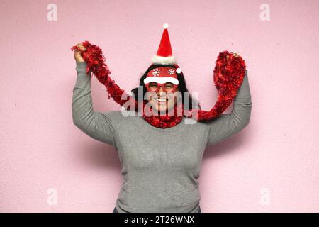 Junge Körper positive fette Latina Frau mit Weihnachtsmütze und -Brille zeigt ihre Begeisterung für die Ankunft im Dezember und Weihnachten Stockfoto