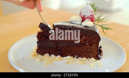 Man Hand nimmt einen Happen von feuchtem, leckerem Schokoladenkuchen mit einem Löffel Stockfoto