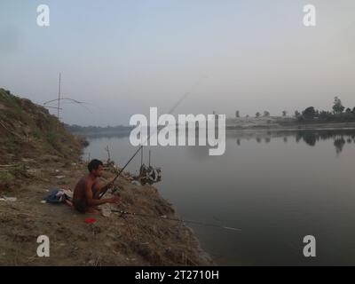 Naogaon, Bangladesch. Oktober 2023. Ein Mann, der während des Sonnenuntergangs im Fluss Atrai fischt. Flusserosion und Landschlupf in der Nähe des Dorfes Shimultoli am Ufer des Flusses Atrai im Bezirk Dhamoirhat Upazila Naogaon. Ungewöhnliche Regenmuster und Überschwemmungen verursachen Landschlupf in diesem Gebiet in der letzten Monsunsaison. (Kreditbild: © MD Mehedi Hasan/ZUMA Press Wire) NUR REDAKTIONELLE VERWENDUNG! Nicht für kommerzielle ZWECKE! Stockfoto