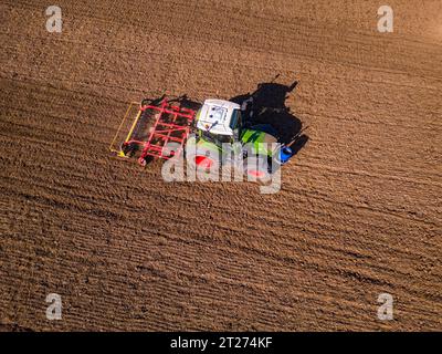 Ein grüner Traktor mit rotem Pflug auf einem Feld mit gepflügtem Boden aus der Vogelperspektive Stockfoto