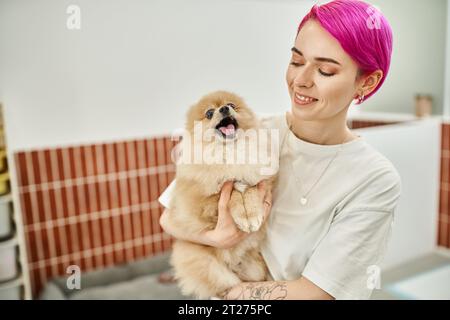 Lächelnde Haustierbetreuerin hält einen schläfrigen und gähnenden Hund in einem einladenden Haustierhotel, hundefreundliches Konzept Stockfoto