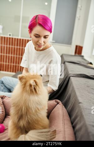 Lächelnder Haustierangestellter, der flauschigen Hund im einladenden Haustierhotel ansieht, Sorgfalt und Zuneigung Stockfoto