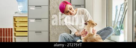 Lächelnder lila-haariger Haussitter kuschelt flauschigen pommerschen Spitz in einem einladenden Haustierhotel, Banner Stockfoto