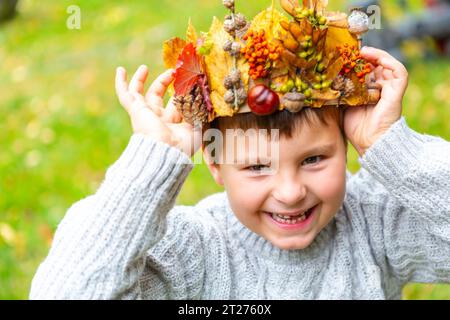 7. Oktober 2023: Der kleine Junge ist glücklich mit einer selbstgemachten Krone aus bunten Blättern und Tannenzapfen. Kind mit Herbstkrone auf dem Kopf im Garten. Spiel- und Bastelkonzept *** kleiner Junge freut sich über eine selbst gebastelte Krone aus bunten Blättern und Tannenzapfen. Kind mit Herbst Krone auf dem Kopf im Garten. Spielen und Basteln Konzept Credit: Imago/Alamy Live News Stockfoto