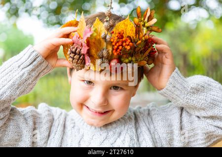 7. Oktober 2023: Der kleine Junge ist glücklich mit einer selbstgemachten Krone aus bunten Blättern und Tannenzapfen. Kind mit Herbstkrone auf dem Kopf im Garten. Spiel- und Bastelkonzept *** kleiner Junge freut sich über eine selbst gebastelte Krone aus bunten Blättern und Tannenzapfen. Kind mit Herbst Krone auf dem Kopf im Garten. Spielen und Basteln Konzept Credit: Imago/Alamy Live News Stockfoto